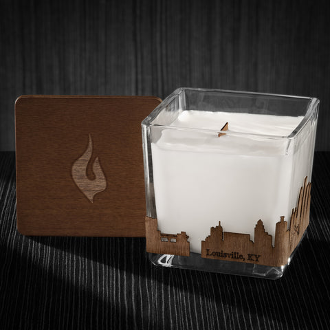 Image of a 3x3x3 soy candle featuring a mahogany scent, crackling wood wick, with a wood lid and a Louisville, KY City skyline wrap design.
