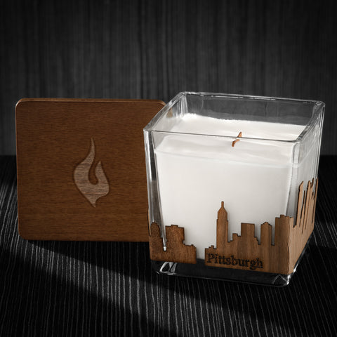 Image of a 3x3x3 soy candle featuring a mahogany scent, crackling wood wick, with a wood lid and a Pittsburgh skyline wrap design.